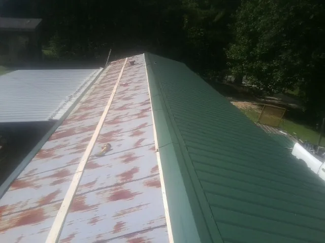 Old rusted panels beside newly installed green metal roofing — Wind Damage Roof Repair by Roofing Brothers in Clark